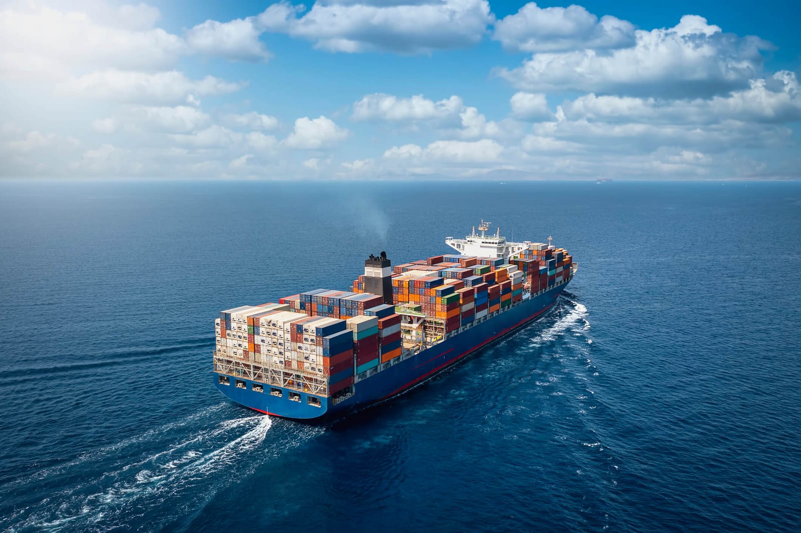 A large container cargo ship travels over calm, blue ocean