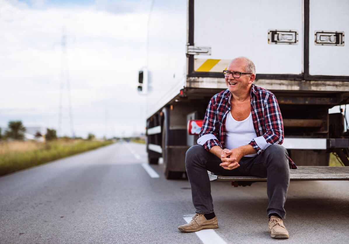 trucker with a red flannel sitting on the back of his truck laughing.