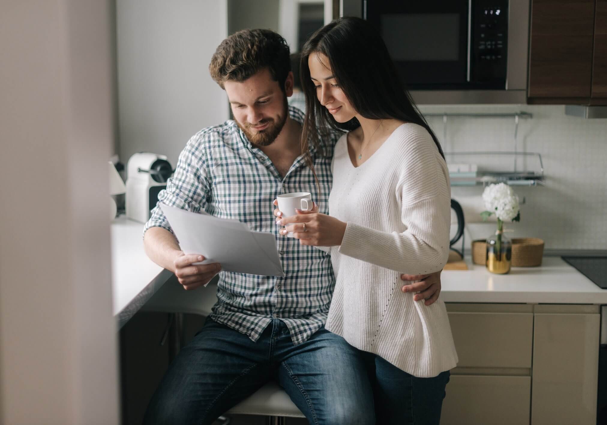 Serious married couple studying mortgage documents together. Beautiful girl holding a cup of coffee in her hands. Daily life of a male and female in apartment.