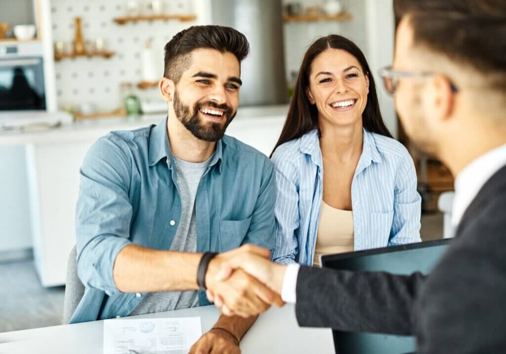 Real estate agent with couple shaking hands closing a deal and signing a contract