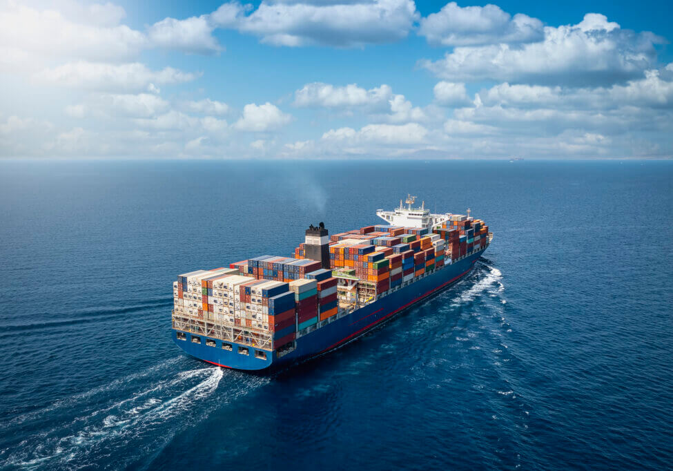 A large container cargo ship travels over calm, blue ocean