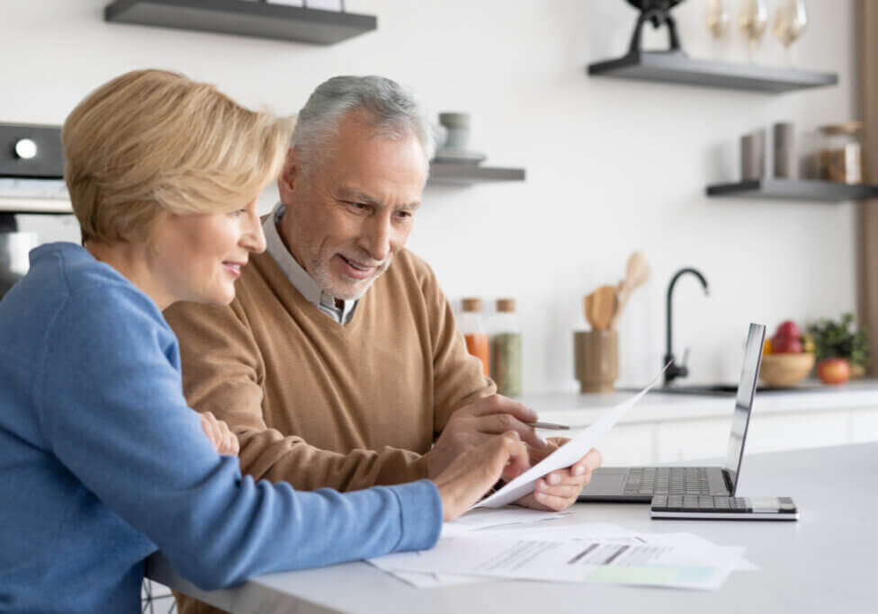 Smiling mature family check utility bills for water supply, gas and electricity, paying online together. Couple filling in quarterly and annual tax forms, calculation of pension savings