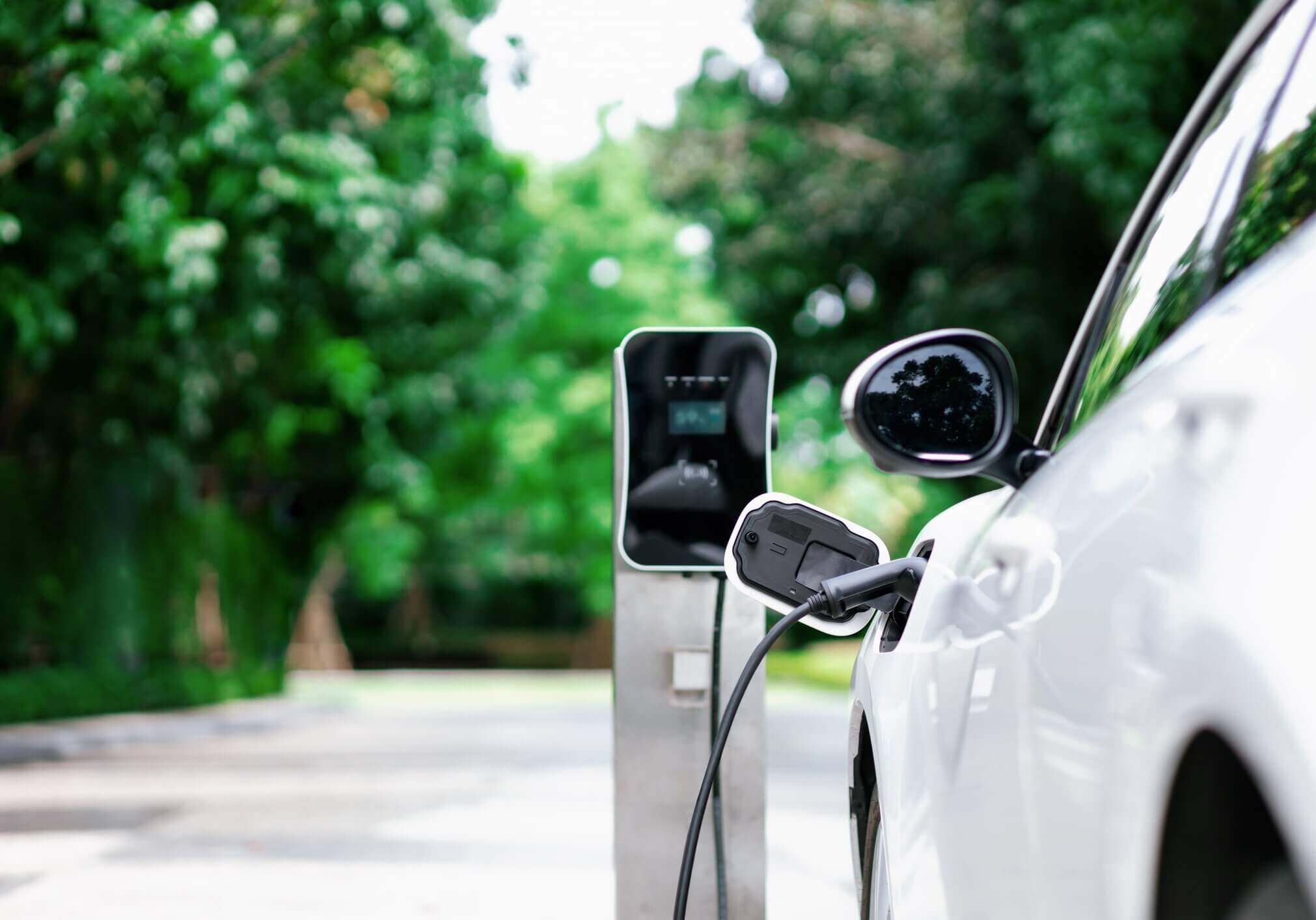 Focus closeup electric vehicle plugged in with EV charger device from blurred background of public charging station powered by renewable clean energy for progressive eco-friendly car concept.