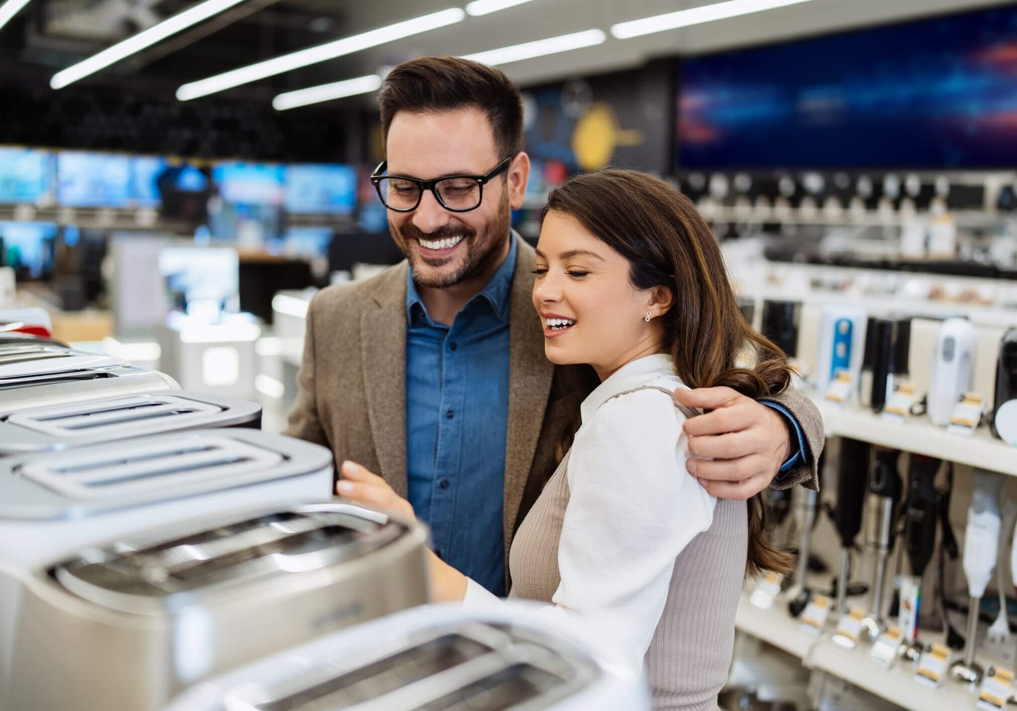 Beautiful and happy middle age couple buying consumer tech products in modern home tech store. They are choosing small kitchen appliances. People and consumerism concept.
