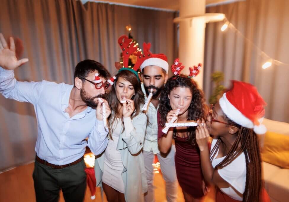 Group of young friends singing, dancing and blowing party whistles at New Year's Eve party