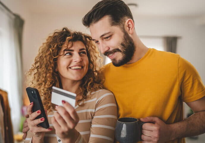 Couple caucasian man and woman husband and wife or boyfriend and girlfriend use mobile phone and credit card shopping online buy stuff or pay make payment booking e-commerce from home real people