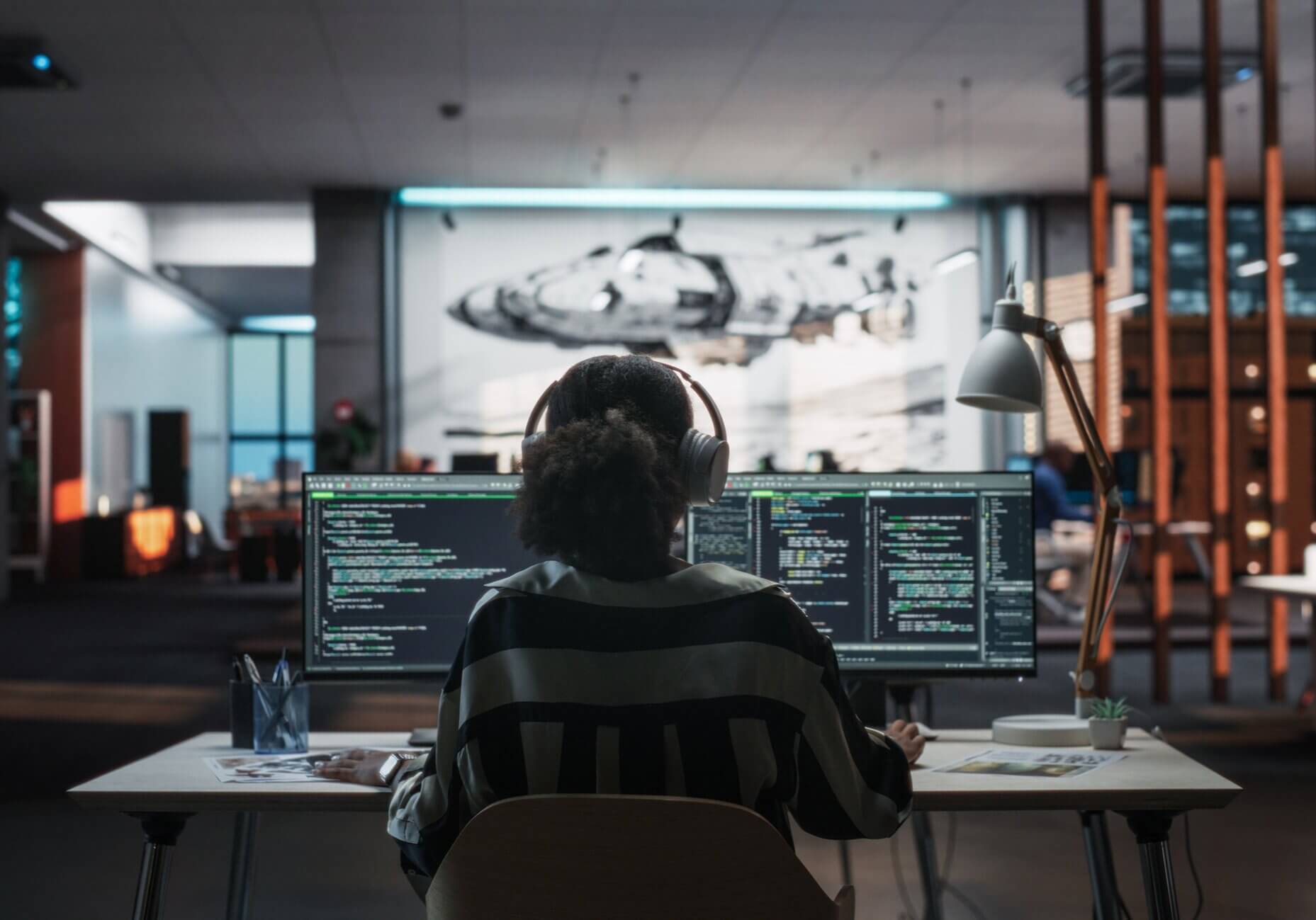 Creative Office: Professional Black Female Programmer Uses Headphones, Working on Desktop Computer. Focused Software Engineer Developing Mobile Applications, Video Games. Listening to Music. Back View